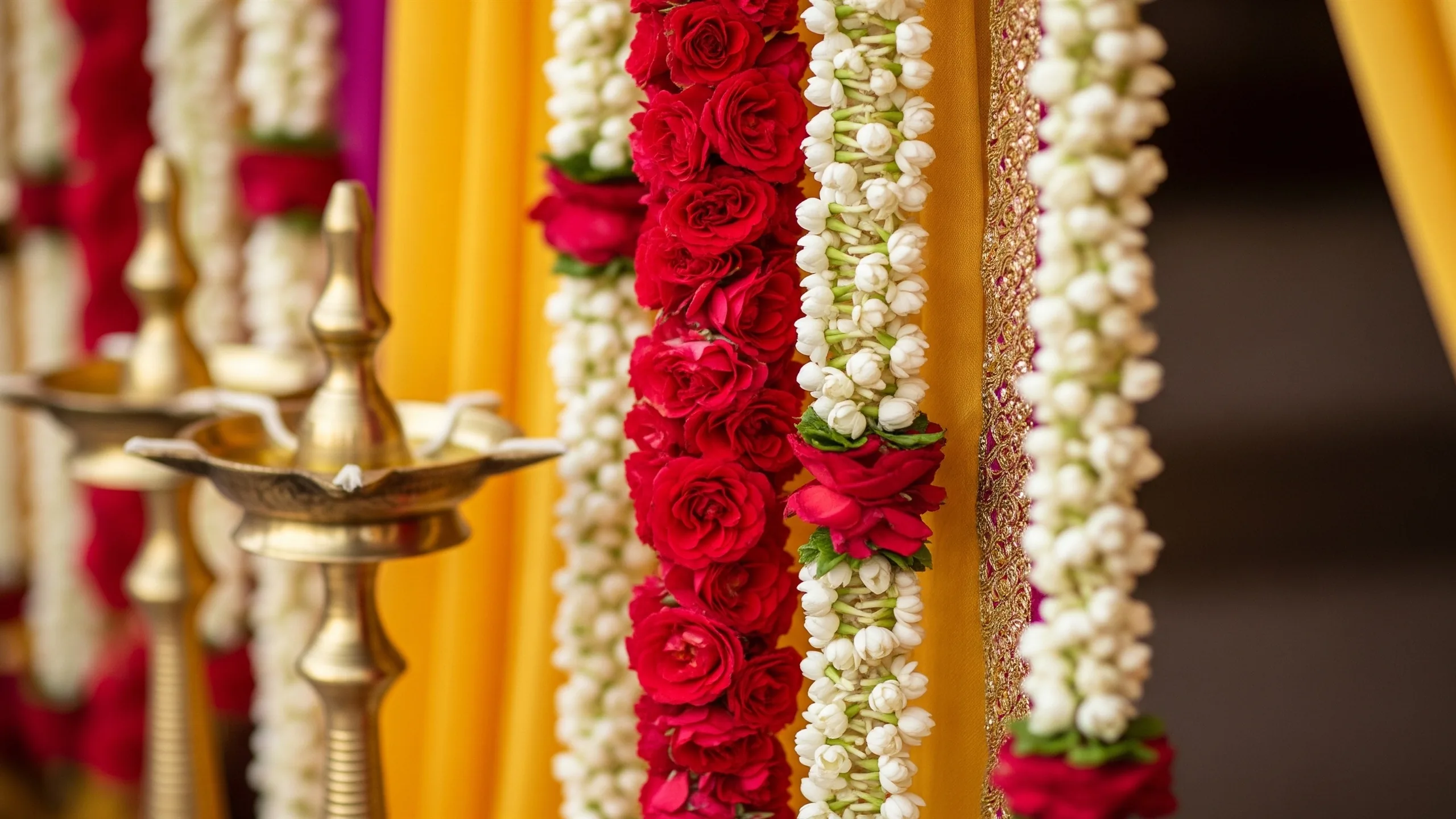 A close detail of premium mandap florals, jasmine strings, rose clusters, carved brass lamps and silk drapery textures, close-up detail